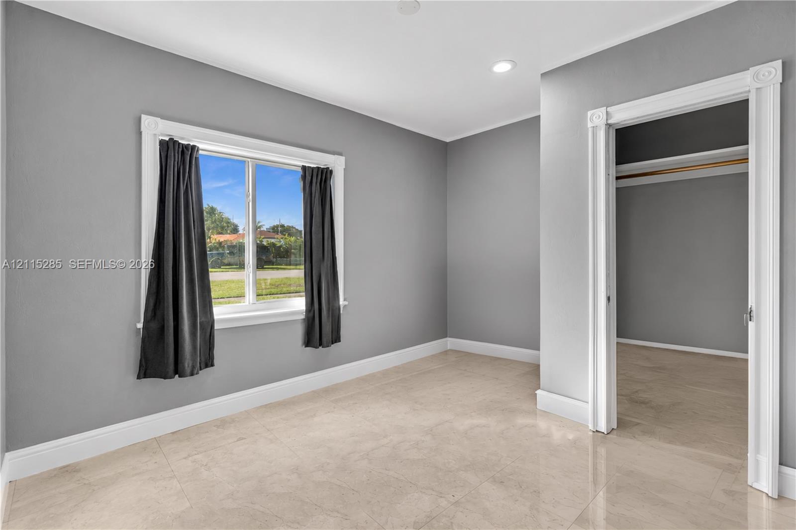 Neutral-toned interior space featuring polished tile flooring, crisp white casing around the doorway and window, and recessed ceiling lighting