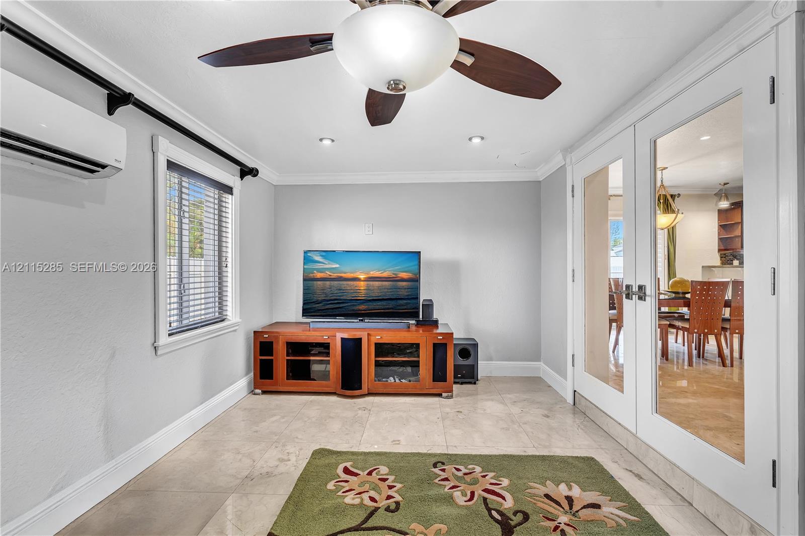 Large-format tile flooring, ceiling fan with integrated lighting, wall-mounted climate control unit, and glass-paneled double doors