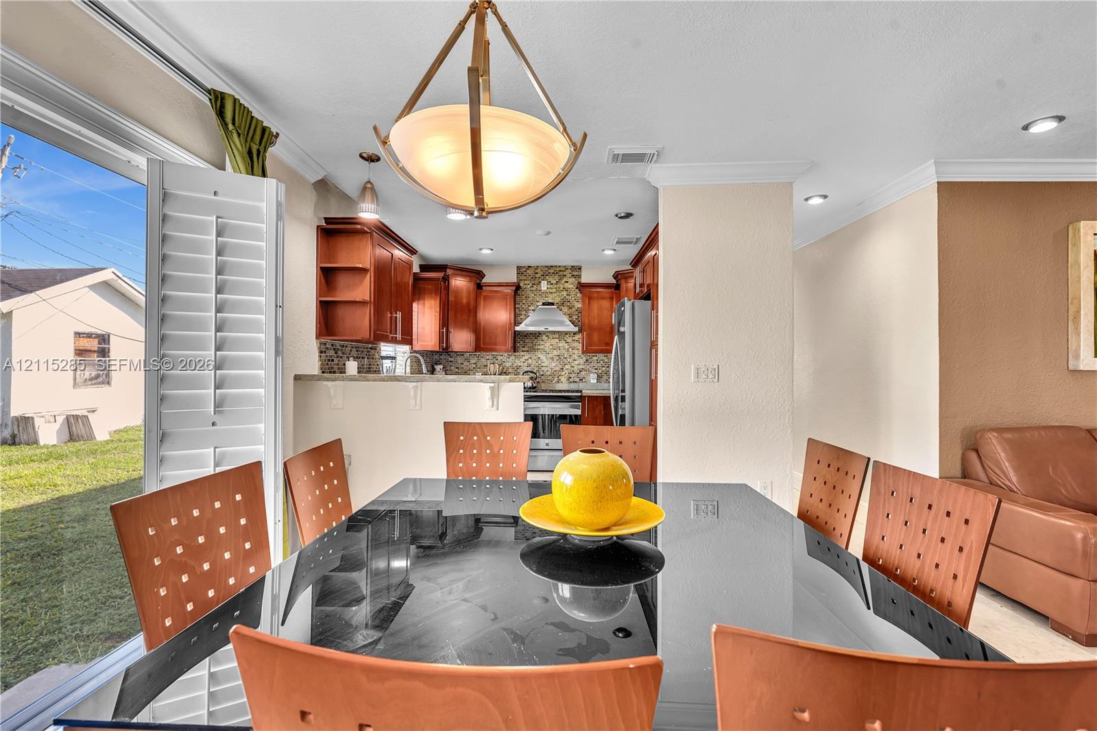 Kitchen featuring wood cabinetry, stone-style backsplash, stainless steel appliances, recessed lighting, and a pendant fixture with a frosted glass shade