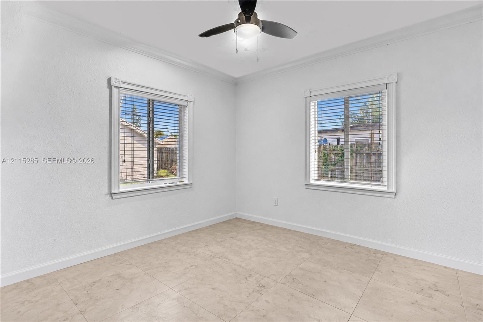 Neutral-toned tile flooring, dual windows with decorative millwork trim, and a ceiling-mounted light fixture with a fan