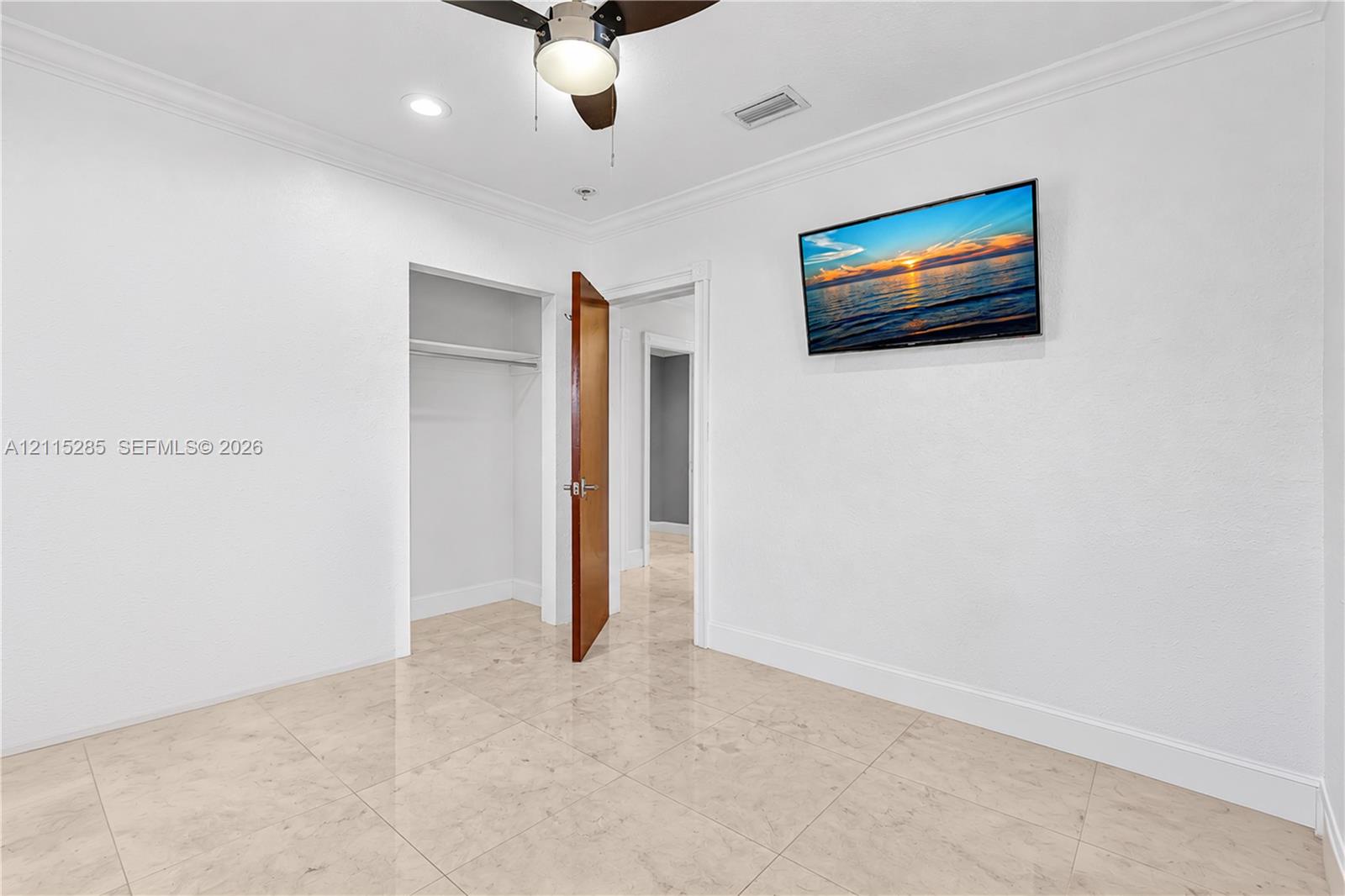 Neutral-toned tile flooring, crown molding, ceiling fan with integrated lighting, and built-in closet storage
