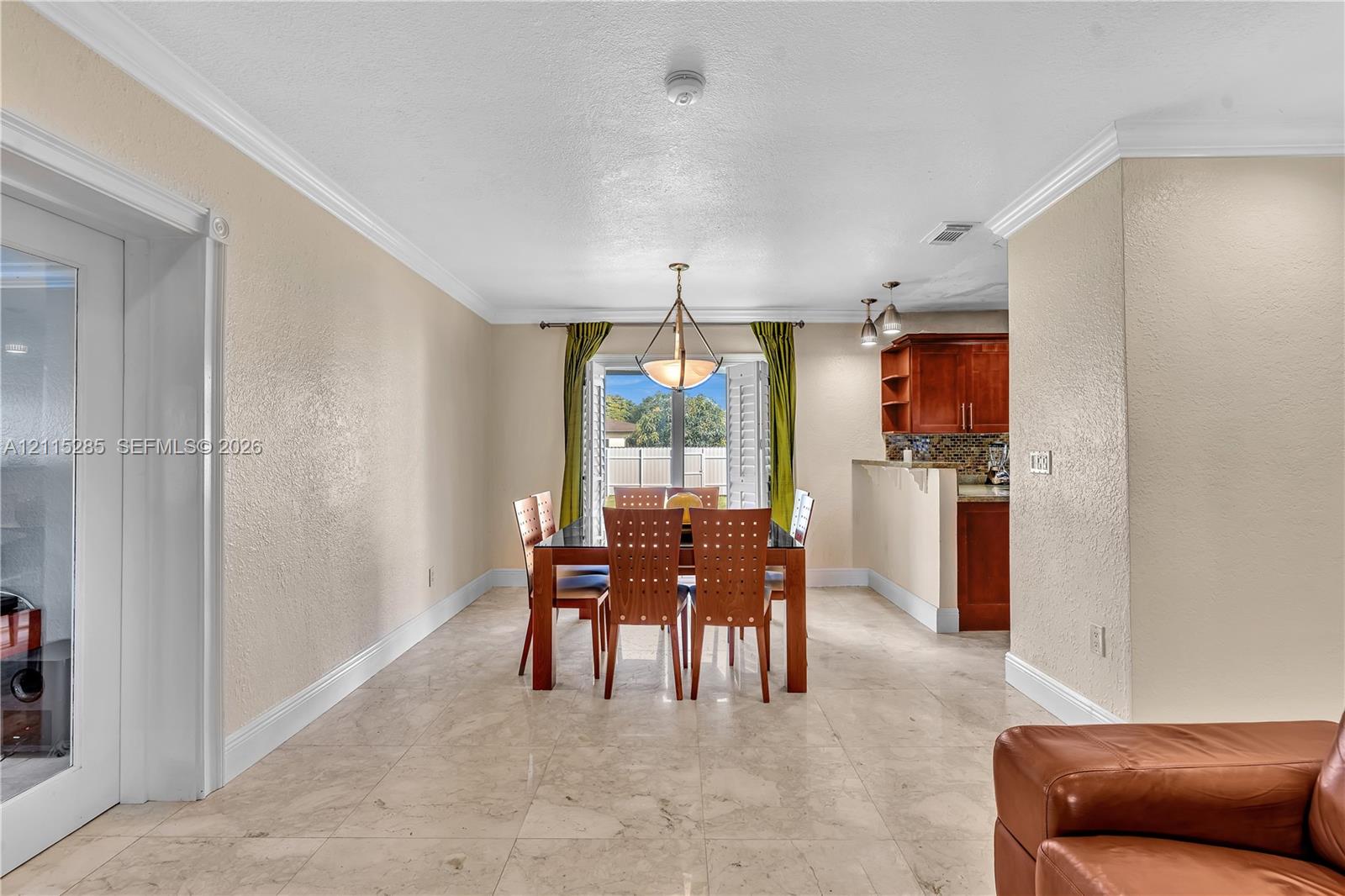 Open-concept interior featuring large-format tile flooring, crown molding, a multi-light pendant fixture, and glass-paneled french doors