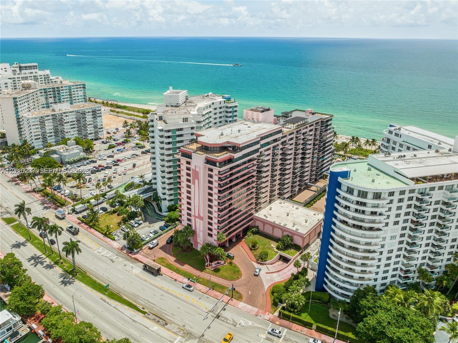 Aerial perspective of coastal high-rise building featuring private balconies, paver-stone driveway, landscaped grounds, and immediate proximity to the oceanfront