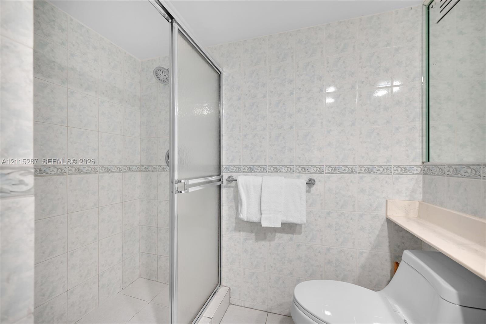 Walk-in shower featuring a sliding glass enclosure, floor-to-ceiling ceramic tile wall finishes, decorative tile accent banding, and a wall-mounted vanity shelf