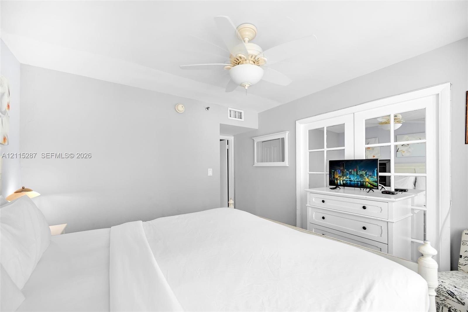 Neutral-toned interior featuring a ceiling fan with integrated lighting and double glass-paneled closet doors