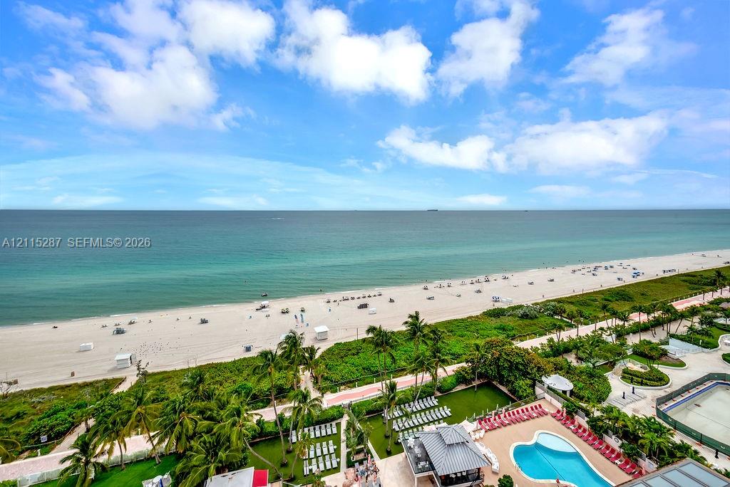 Elevated oceanfront perspective featuring an expansive sandy beach, tropical landscaping, and a large custom-shaped swimming pool with surrounding terrace