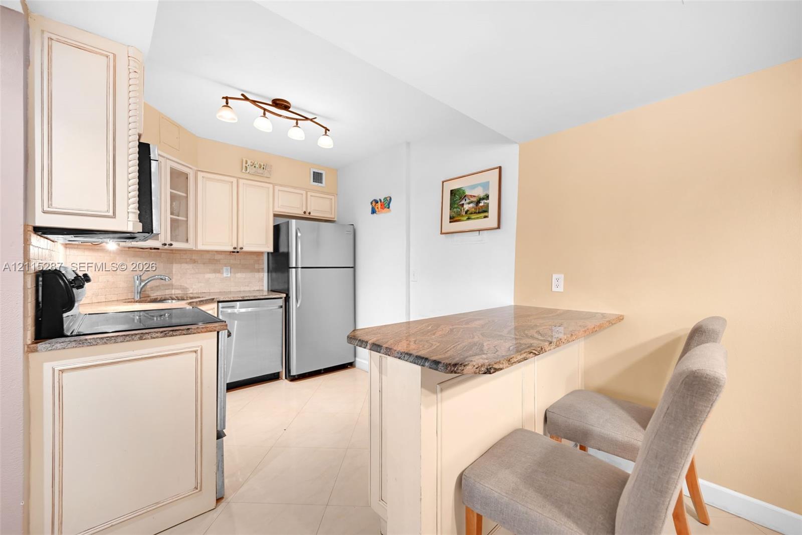 Kitchen featuring custom cabinetry, stone-surfaced countertops, a stone-tiled backsplash, stainless steel appliances, and a breakfast bar