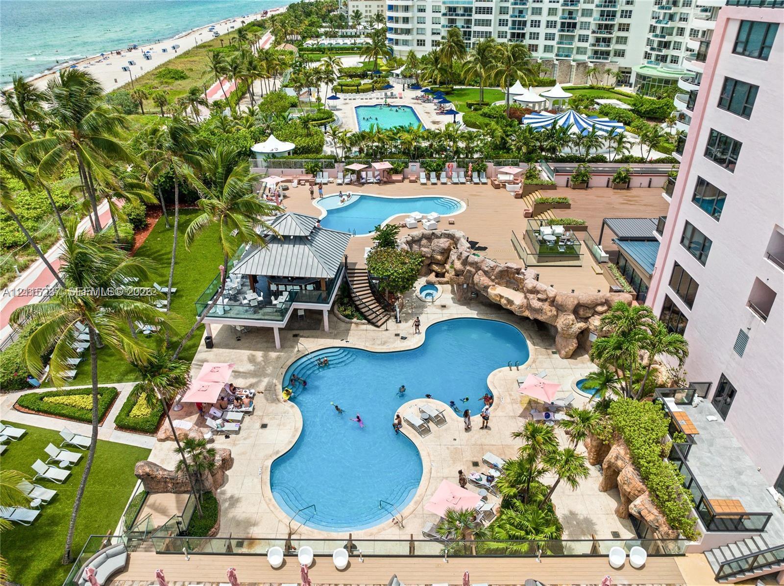 Multi-level swimming pools with rock features, poolside pavilion, integrated hot tub, landscaped grounds, and paved patio surfaces