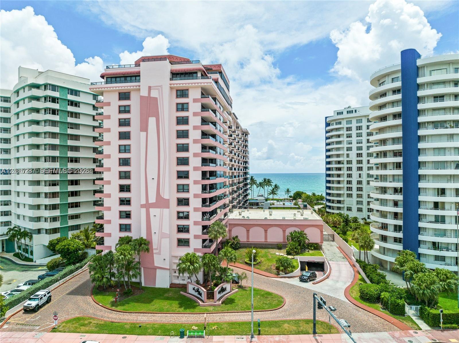 Multi-story residential building exterior featuring private balconies, concrete construction, circular drive, and lush landscaped grounds