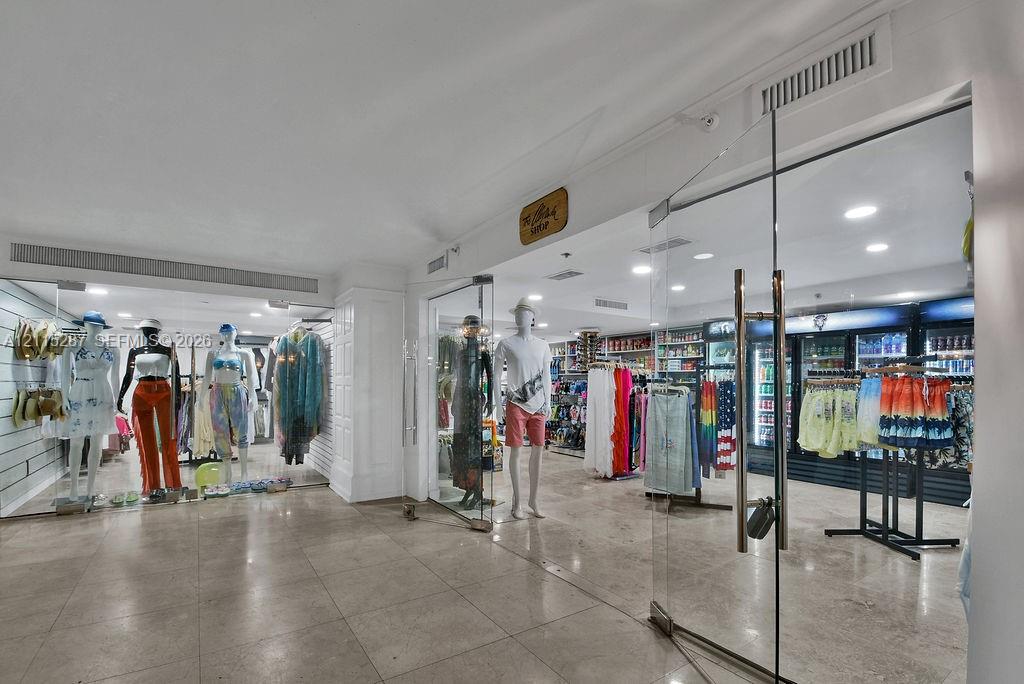 Commercial interior featuring polished stone tile flooring, recessed ceiling lighting, and frameless glass entry doors with metallic hardware