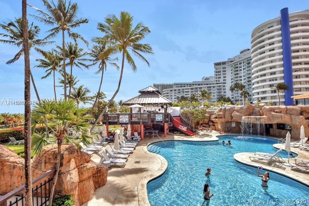 Swimming pool featuring a rock-formation waterfall, a poolside pavilion with a covered structure, and mature palm trees