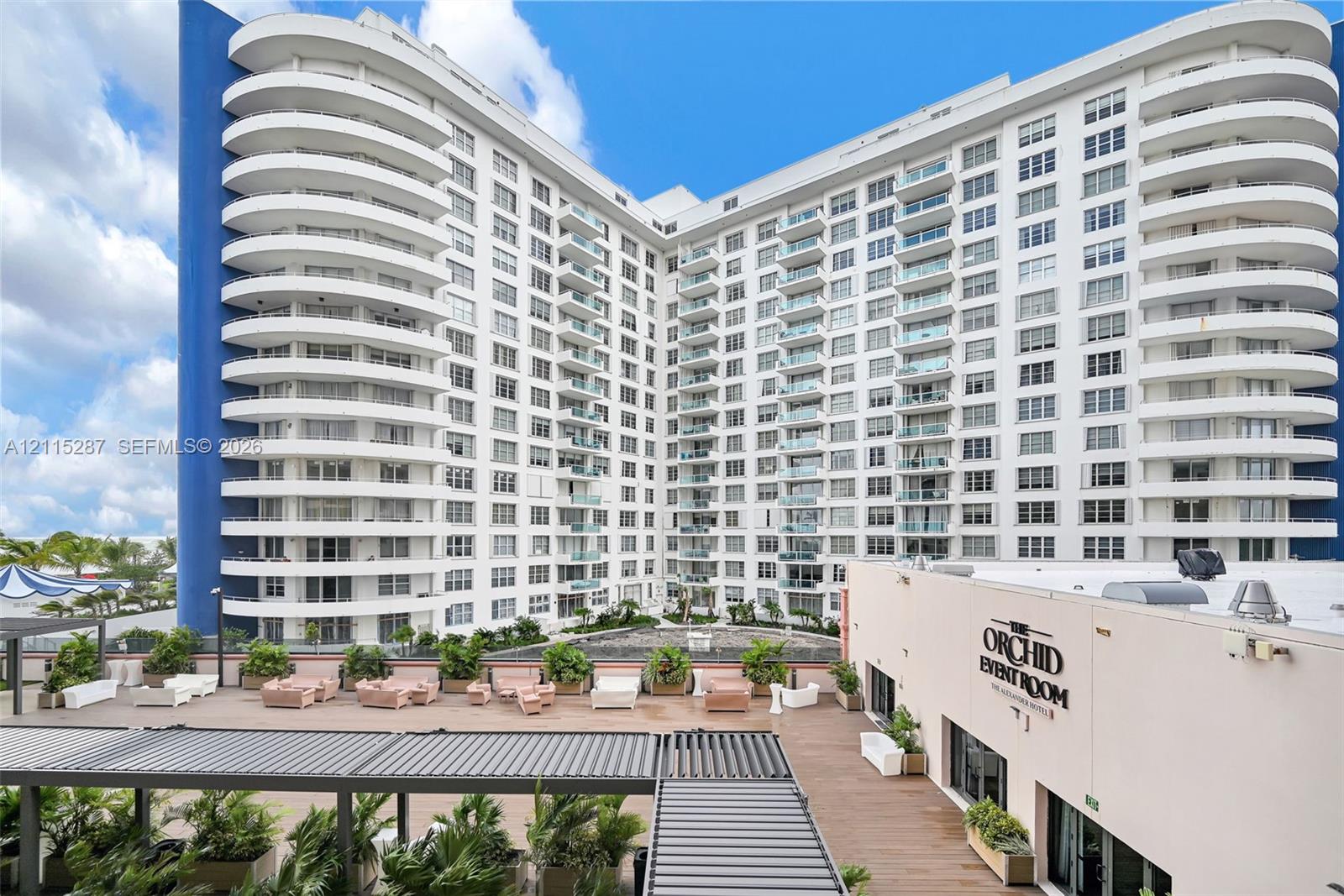 Multi-story high-rise building featuring rounded wrap-around balconies, a structured expansive terrace, integrated metal pergolas, and built-in landscape planters