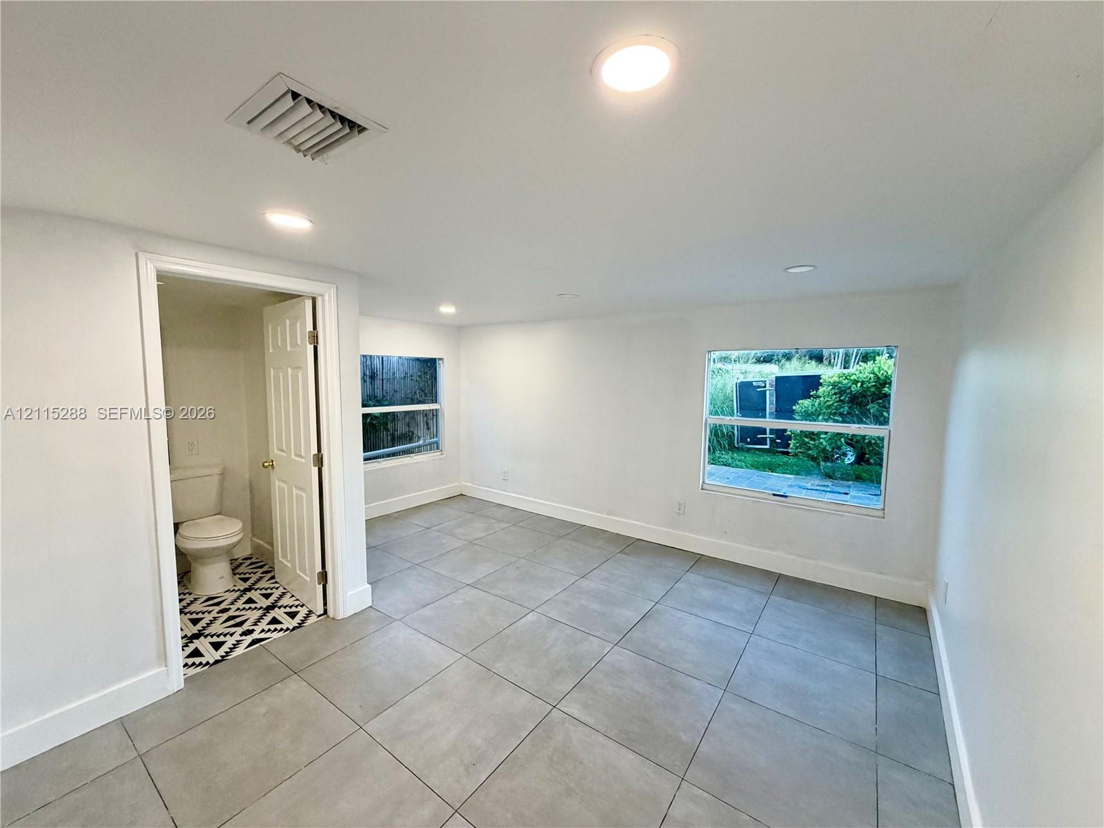 Interior space featuring neutral wall tones, large-format tile flooring, recessed ceiling lighting, and windows with exterior exposure