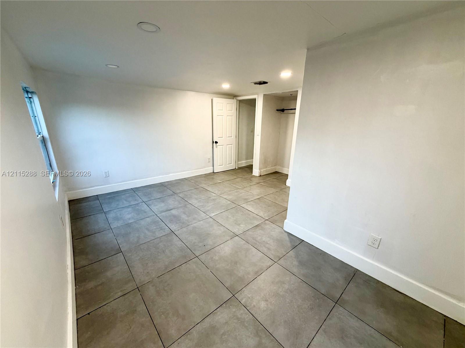 Neutral-toned interior featuring large-format square floor tiles, recessed ceiling lighting, and a walk-in closet with a built-in clothing rod