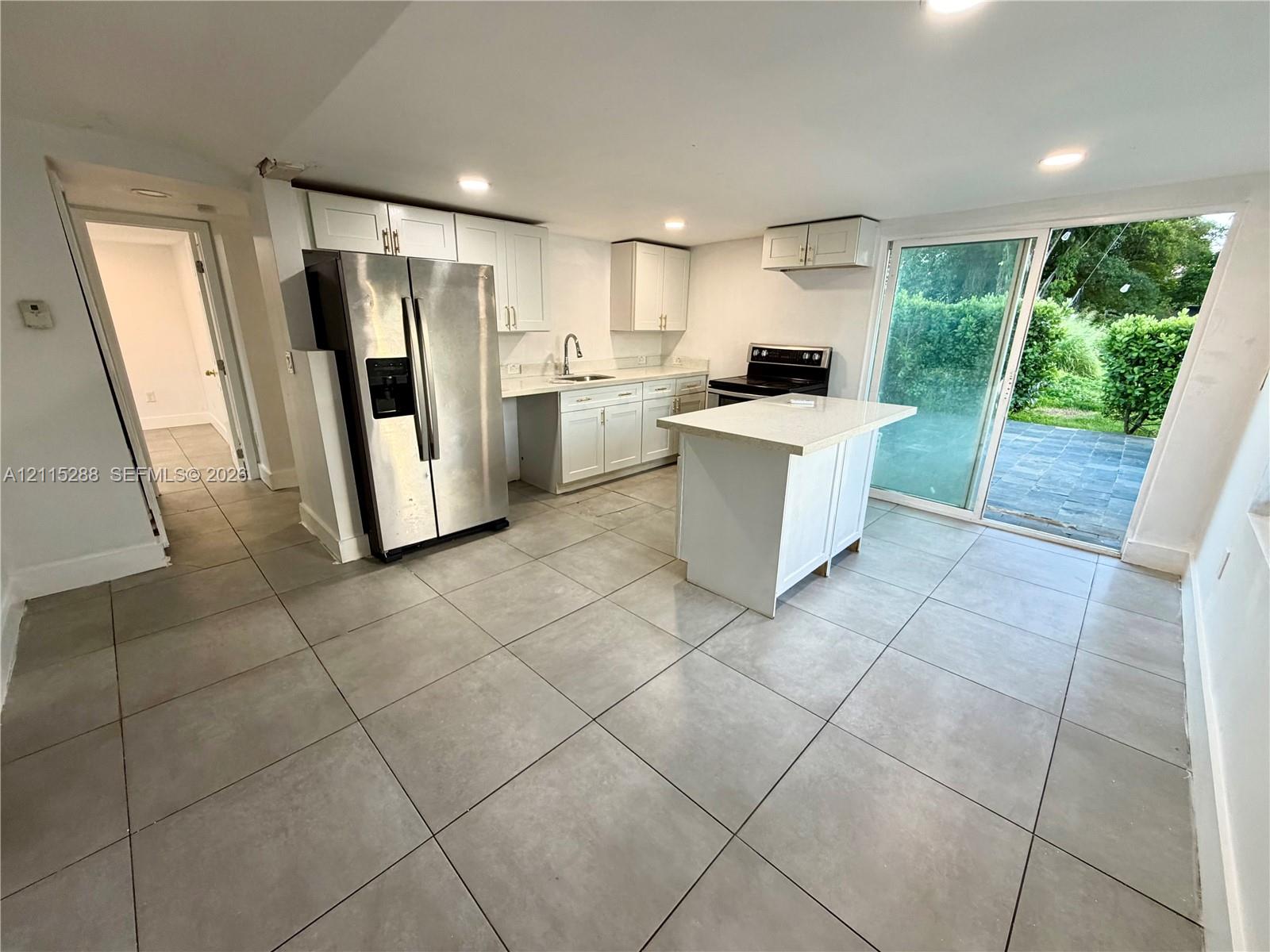 Kitchen featuring white cabinetry, an island with a light-toned countertop, stainless steel refrigerator, tile flooring, and sliding glass doors