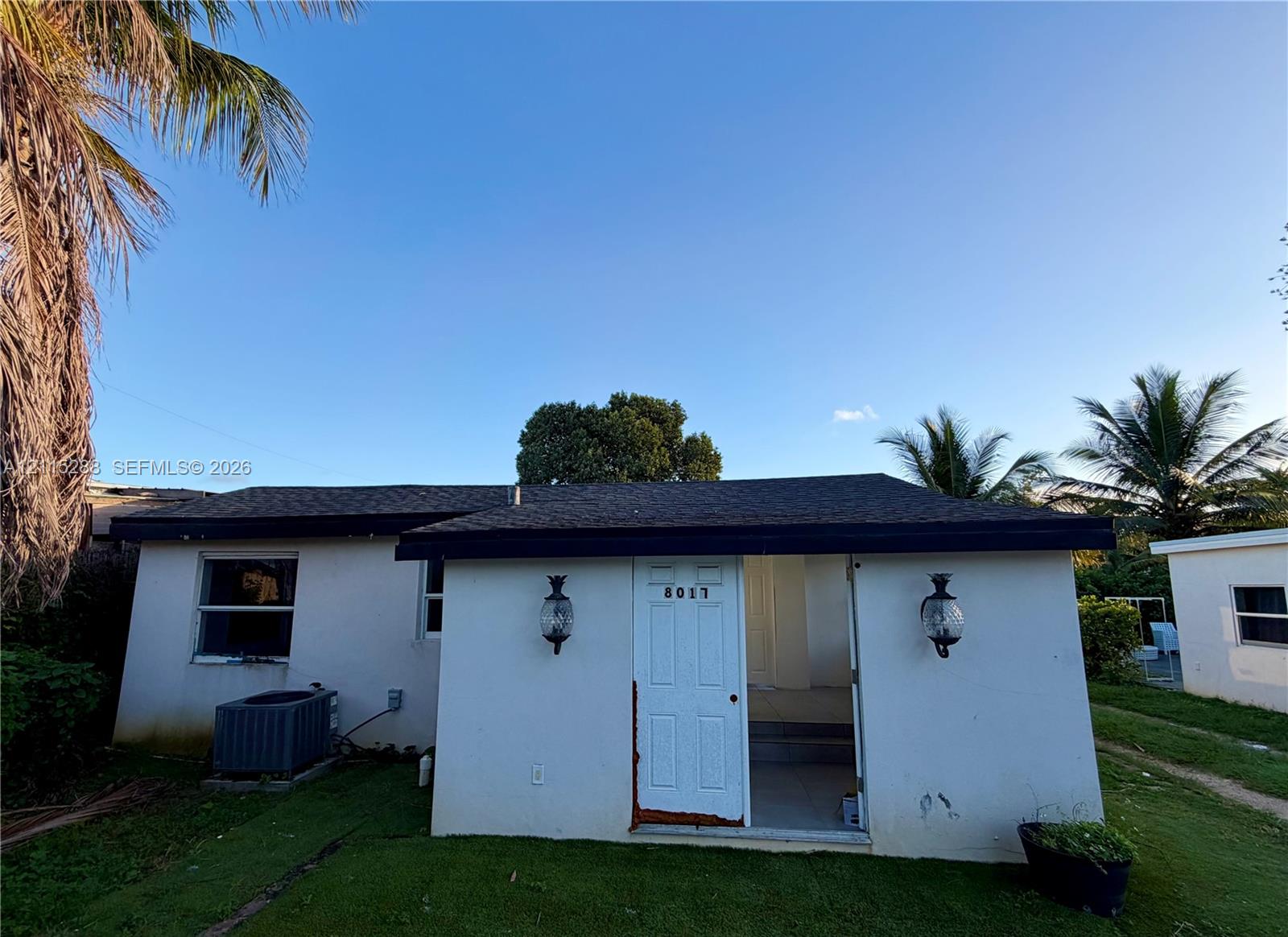 Exterior elevation featuring stucco siding, asphalt shingle roof, dual wall-mounted coach lights, and a lawn