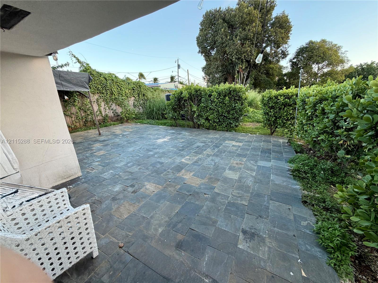 Outdoor patio featuring natural stone tile flooring, covered overhang, and perimeter shrubbery