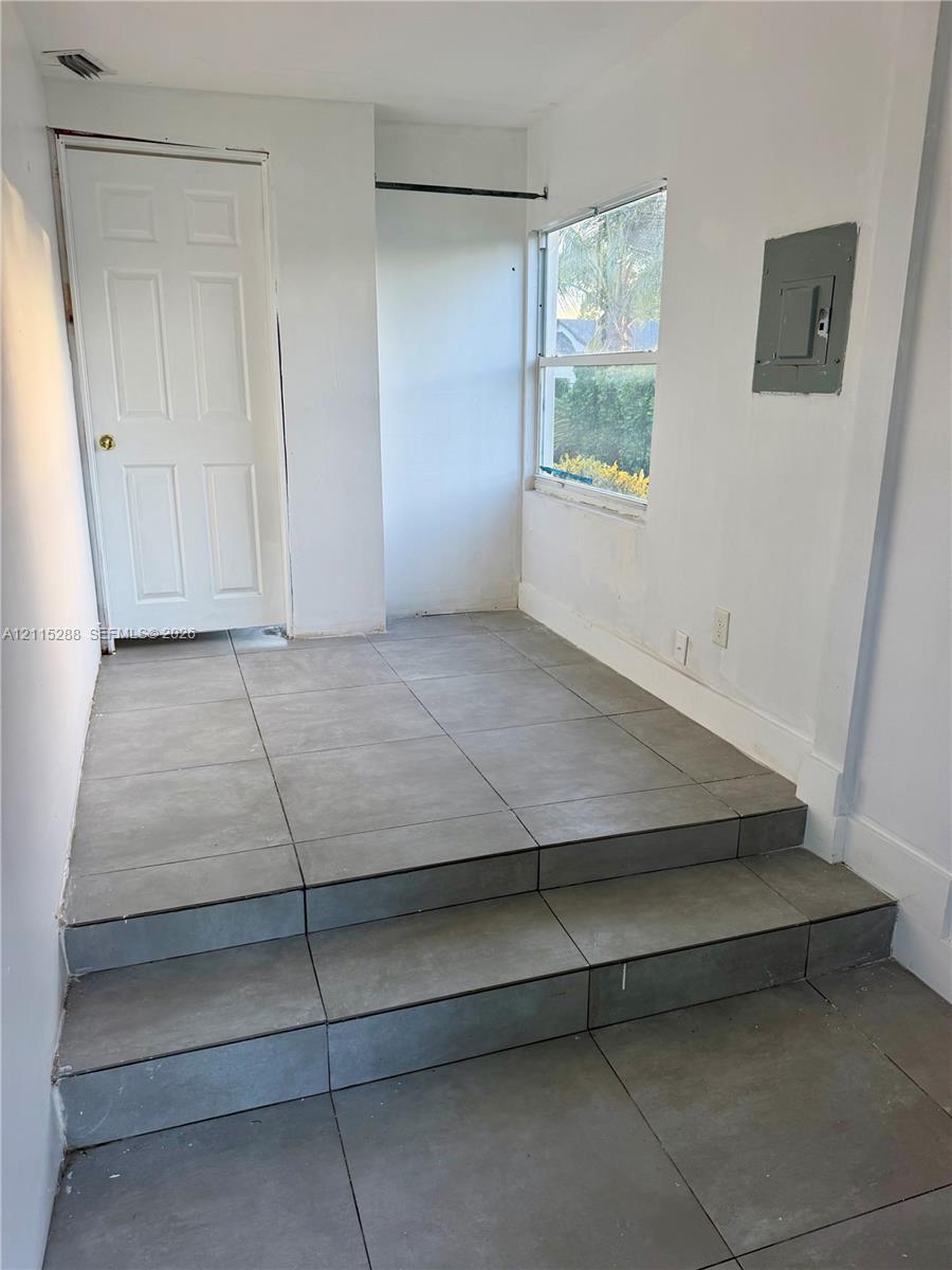 Interior space featuring large-format grey tile flooring, a multi-level stepped transition, a single-panel interior door, and a horizontal window