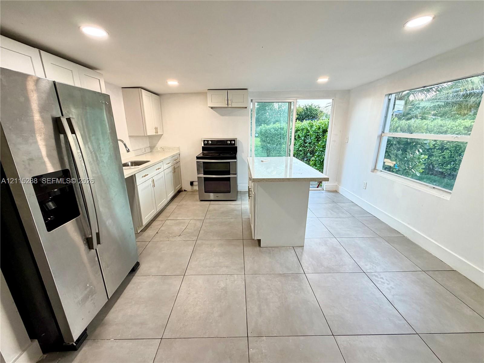Kitchen featuring white shaker-style cabinetry, a central island with a stone countertop, large-format tile flooring, stainless steel appliances, and recessed lighting