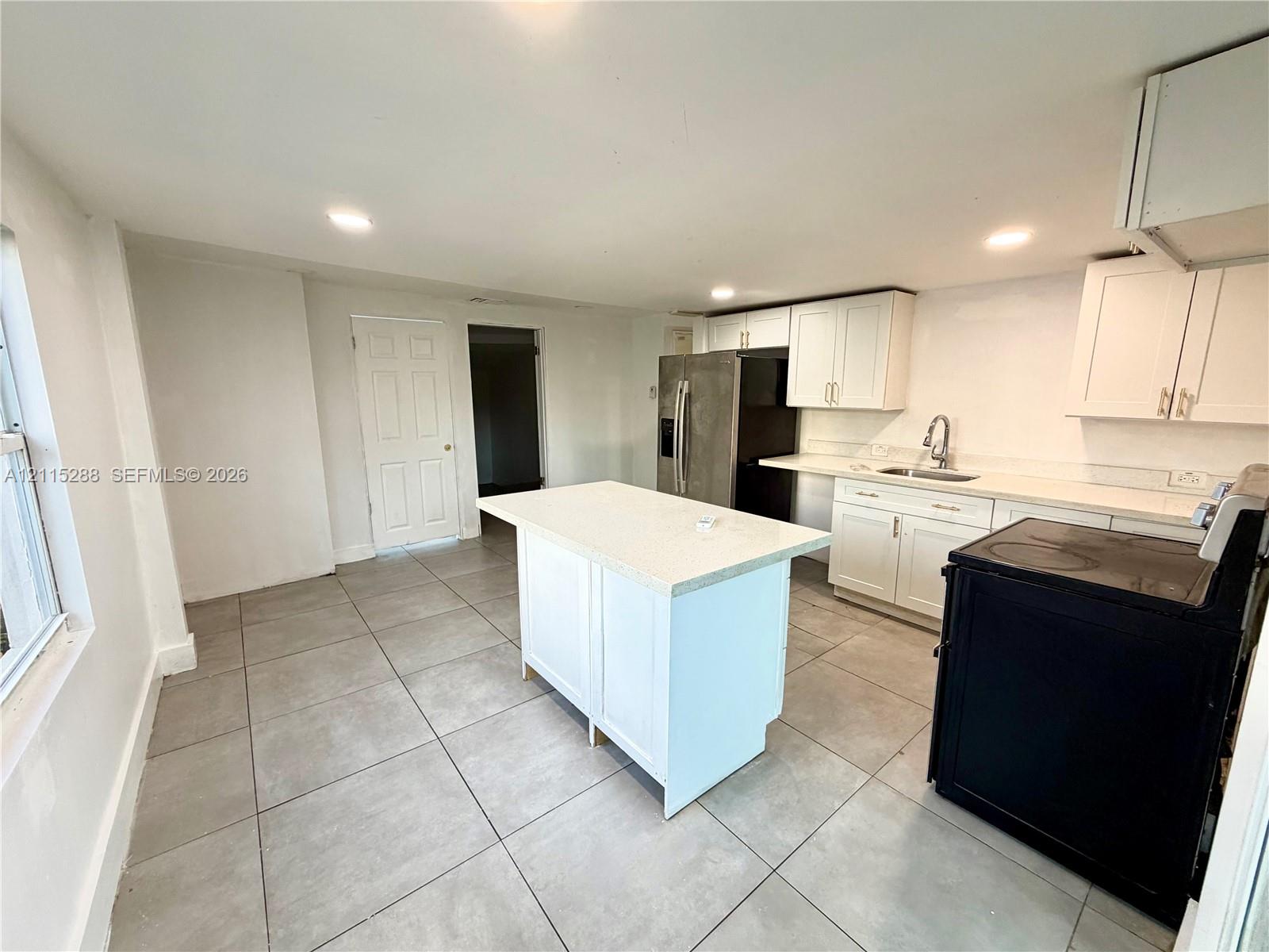 Kitchen featuring white shaker-style cabinetry, quartz countertops, a central island, recessed lighting, and tile flooring