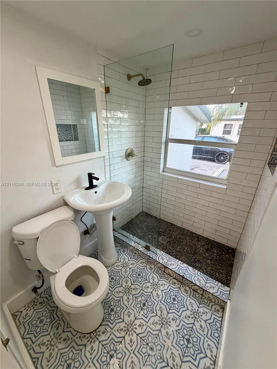 Walk-in shower featuring glass paneling, pebble-stone flooring, and subway tile wall surrounds