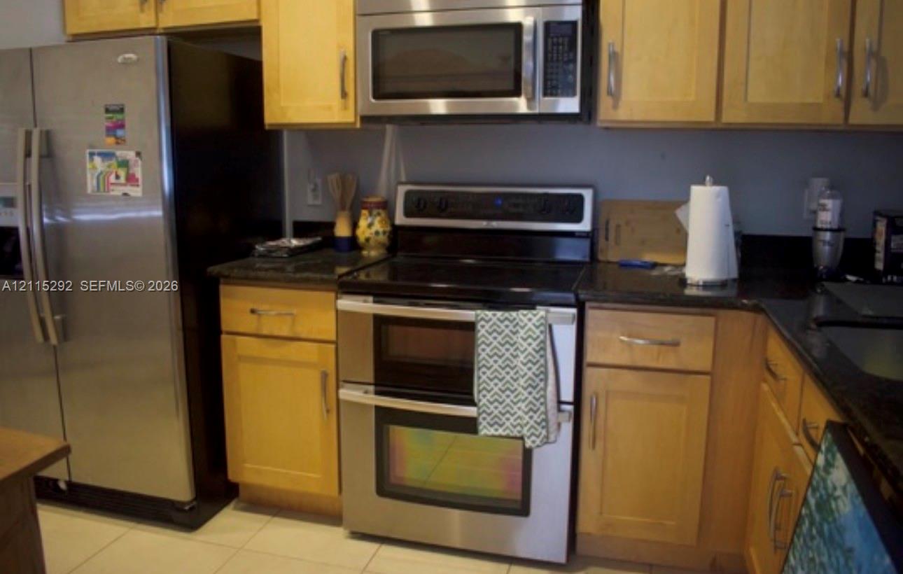 Kitchen featuring light-finish wood cabinetry, dark stone countertops, stainless steel side-by-side refrigerator, stainless steel double oven, and stainless steel over-the-range microwave