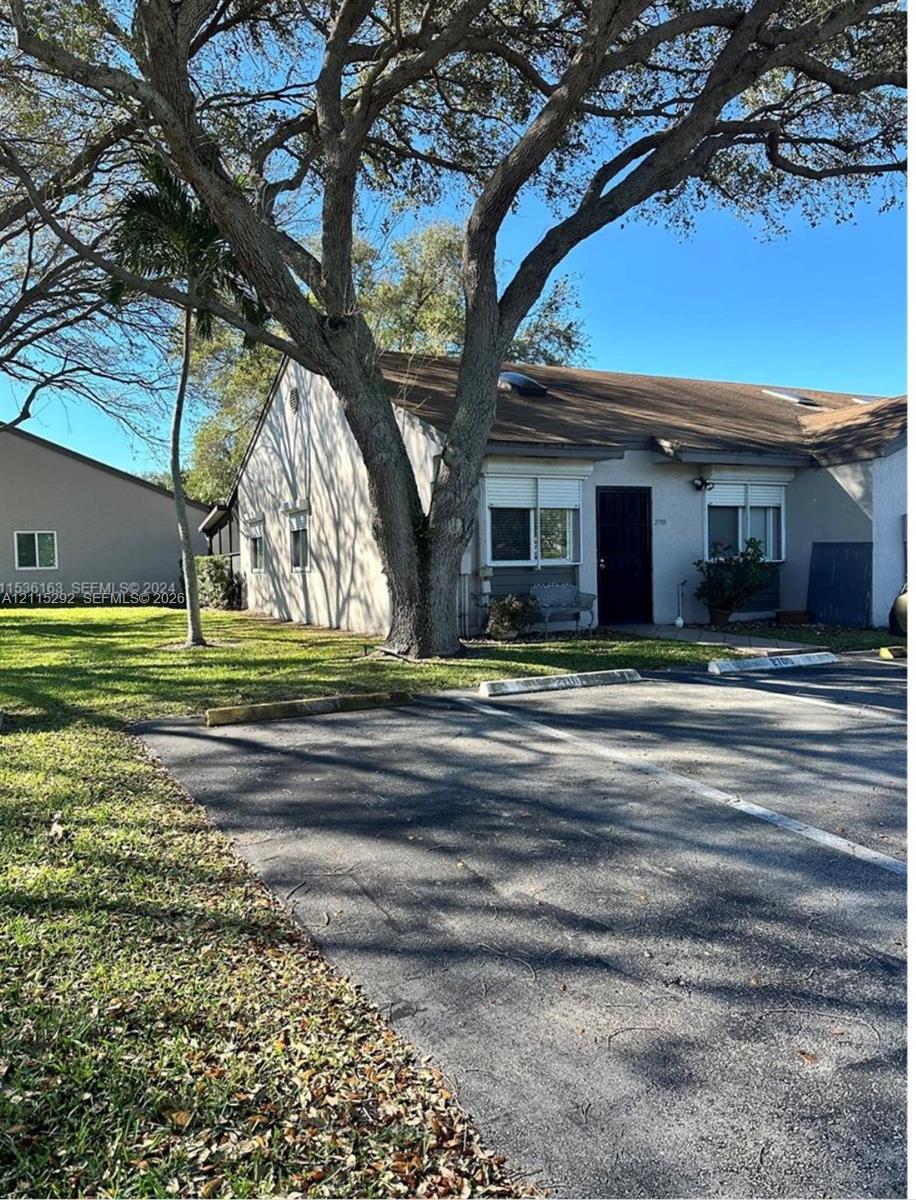 Single-story exterior featuring a shingled roof, stucco siding, multi-pane windows, and a paved parking area with designated stalls