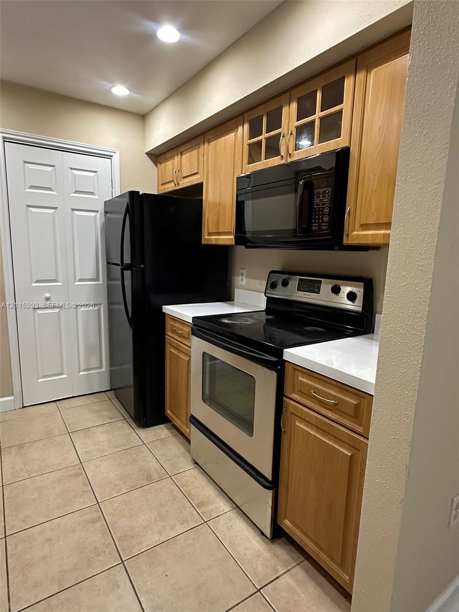 Kitchen featuring wood-finish cabinetry, solid surface countertops, a stainless steel range, a built-in microwave, and tile flooring