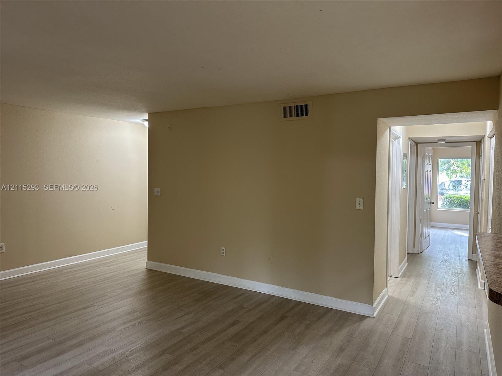 Interior space featuring wood-finish flooring and neutral wall tones, punctuated by a passage with a doorway leading to natural exterior light