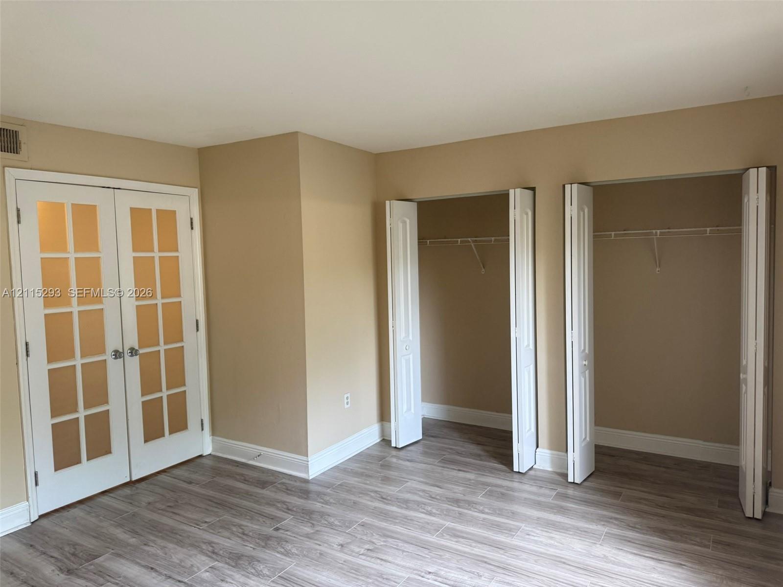 Double French doors with glass panes, wood-finish flooring, and two reach-in closets featuring bi-fold doors and built-in shelving