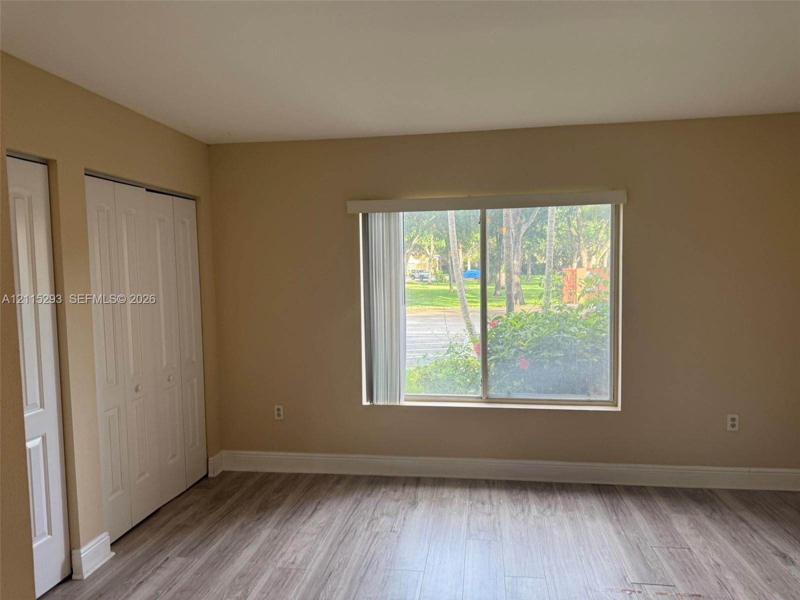 Interior room featuring wood-finish flooring, a large sliding window, and two sets of bi-fold closet doors