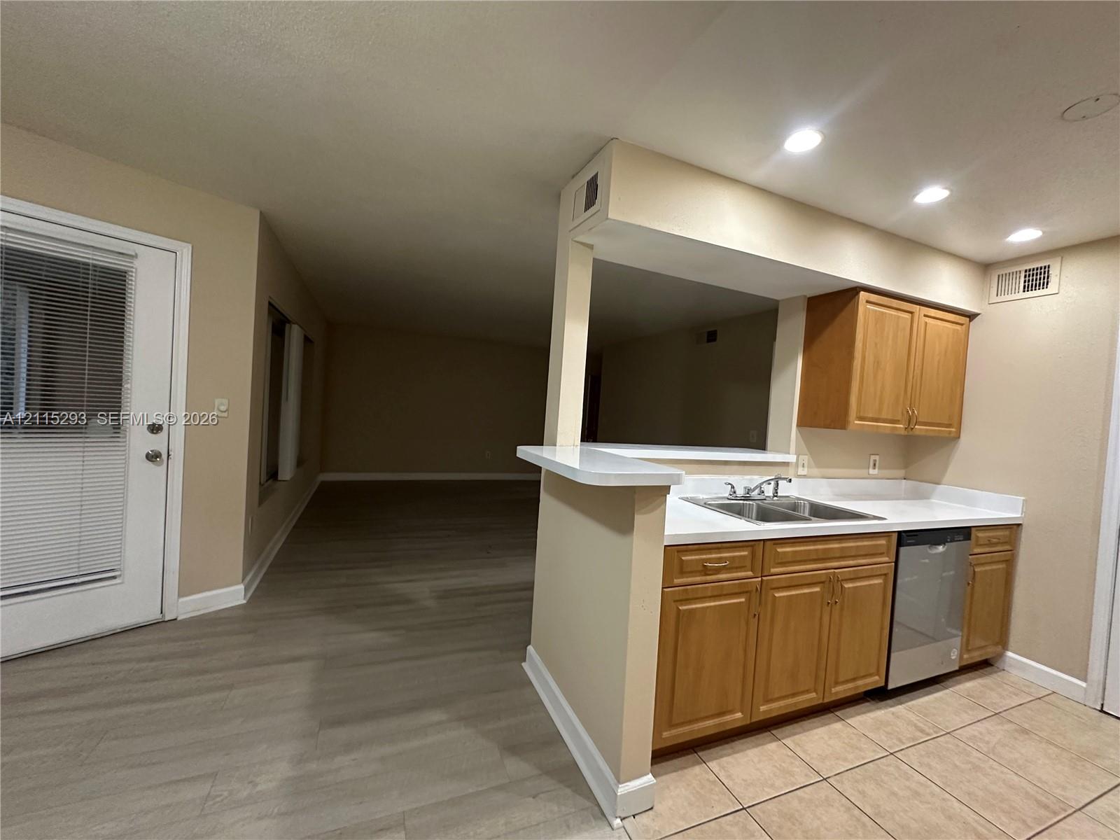 Kitchen featuring light-finish cabinetry, solid-surface countertops, a dual-basin stainless steel sink, a stainless steel dishwasher, and tile flooring