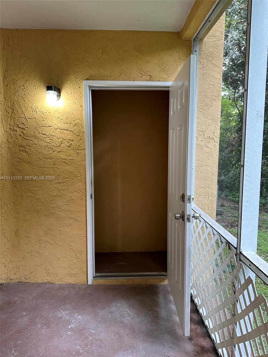 Enclosed porch featuring textured stucco walls, exterior wall-mounted lighting, and a storage closet with a six-panel door, bordered by white lattice screening