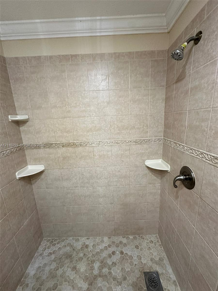 Shower enclosure featuring floor-to-ceiling tile, decorative accent trim, integrated corner shelving, hexagonal floor tiling, and wall-mounted metal fixtures
