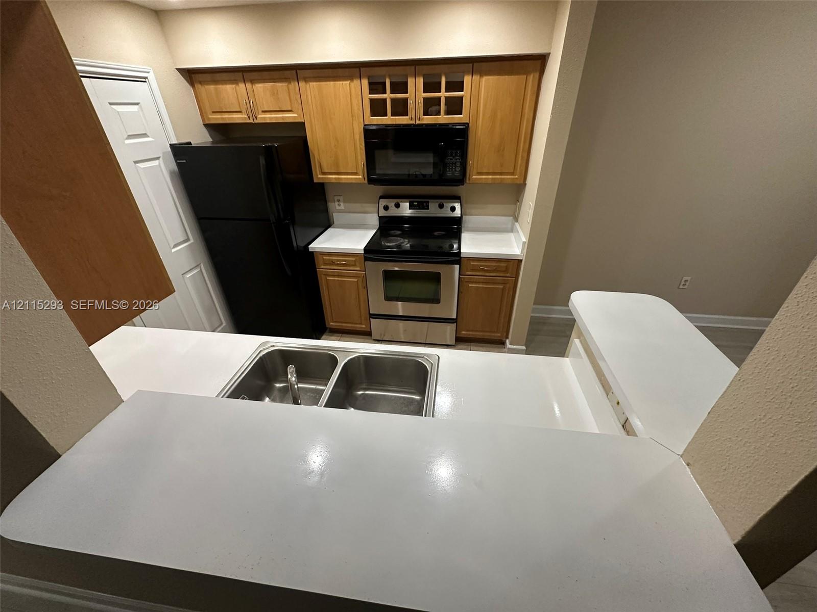 Kitchen featuring wood cabinetry, solid-surface countertops with a breakfast bar, a stainless steel electric range, and a double-basin stainless steel sink