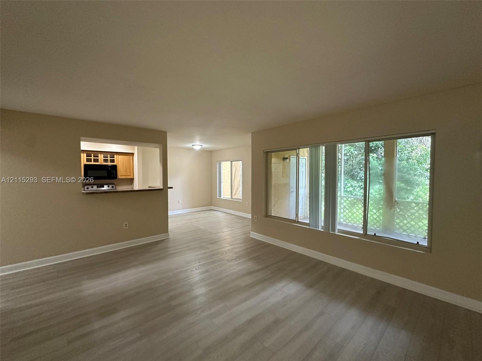 Interior featuring wood-finish flooring, a large picture window, and a pass-through opening to the kitchen area