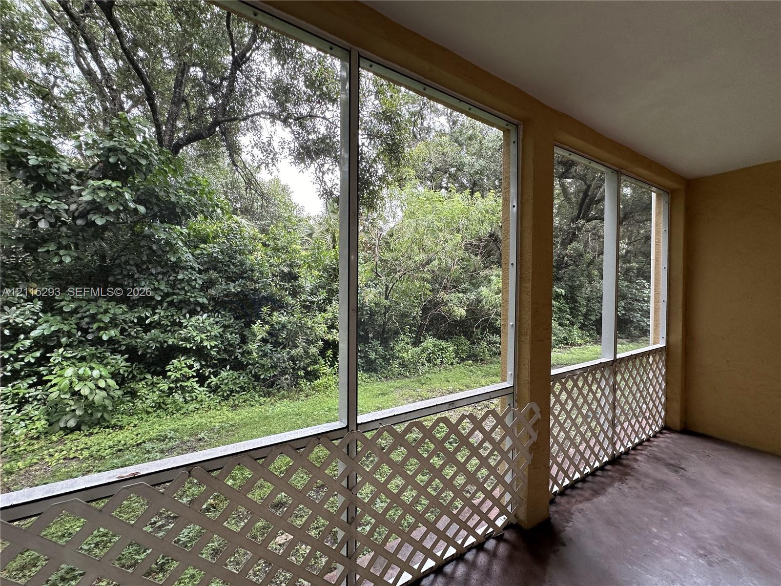 Screened-in porch featuring concrete flooring, full-height window screening, and white lattice decorative panels