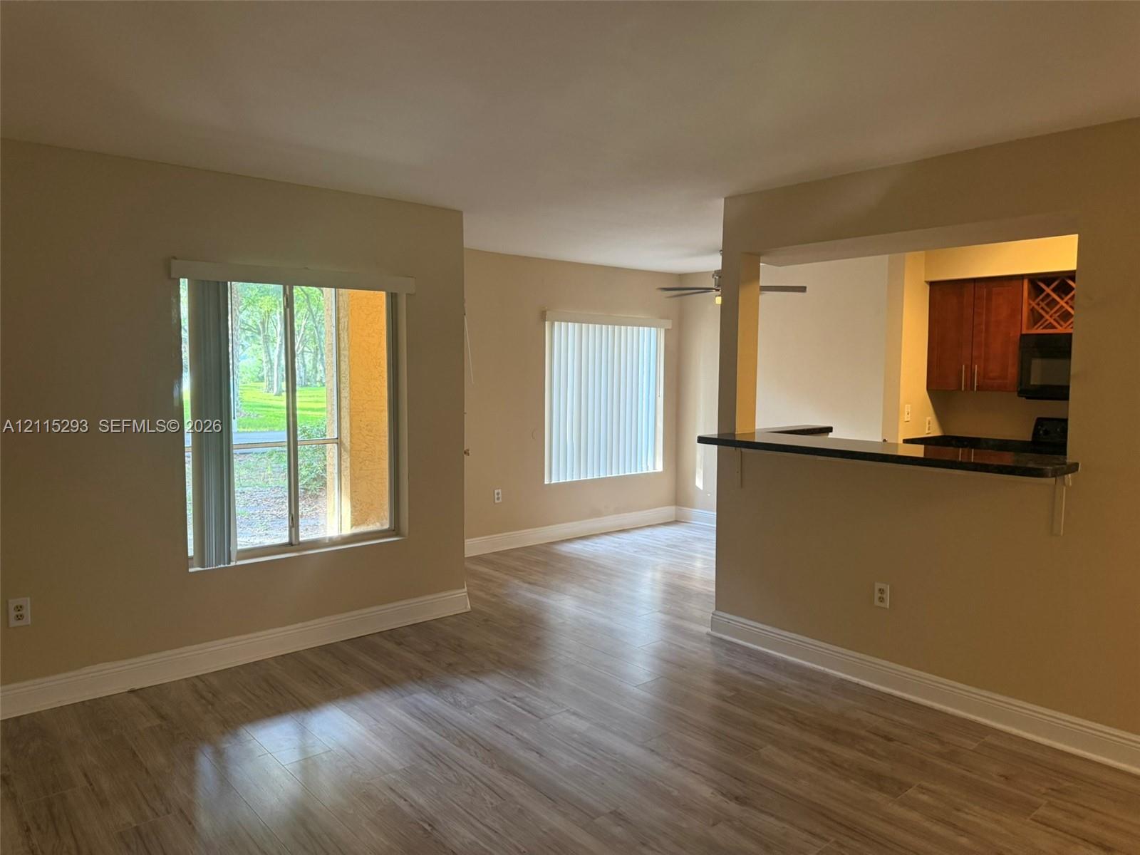 Living area featuring wood-finish flooring, a pass-through opening, dark-toned kitchen cabinetry, a breakfast bar, and multiple windows