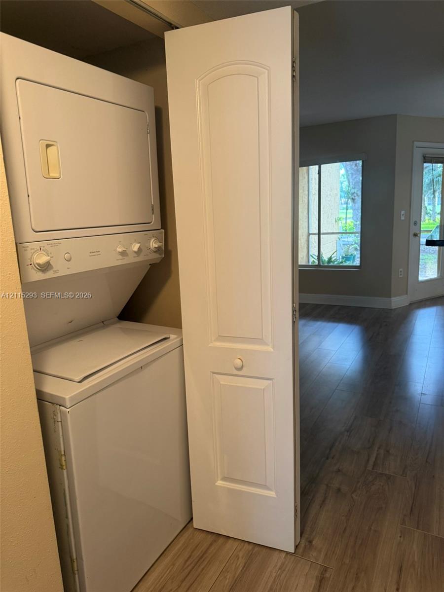 Stacked laundry unit enclosed by a two-panel hinged door, featuring wood-finish flooring throughout