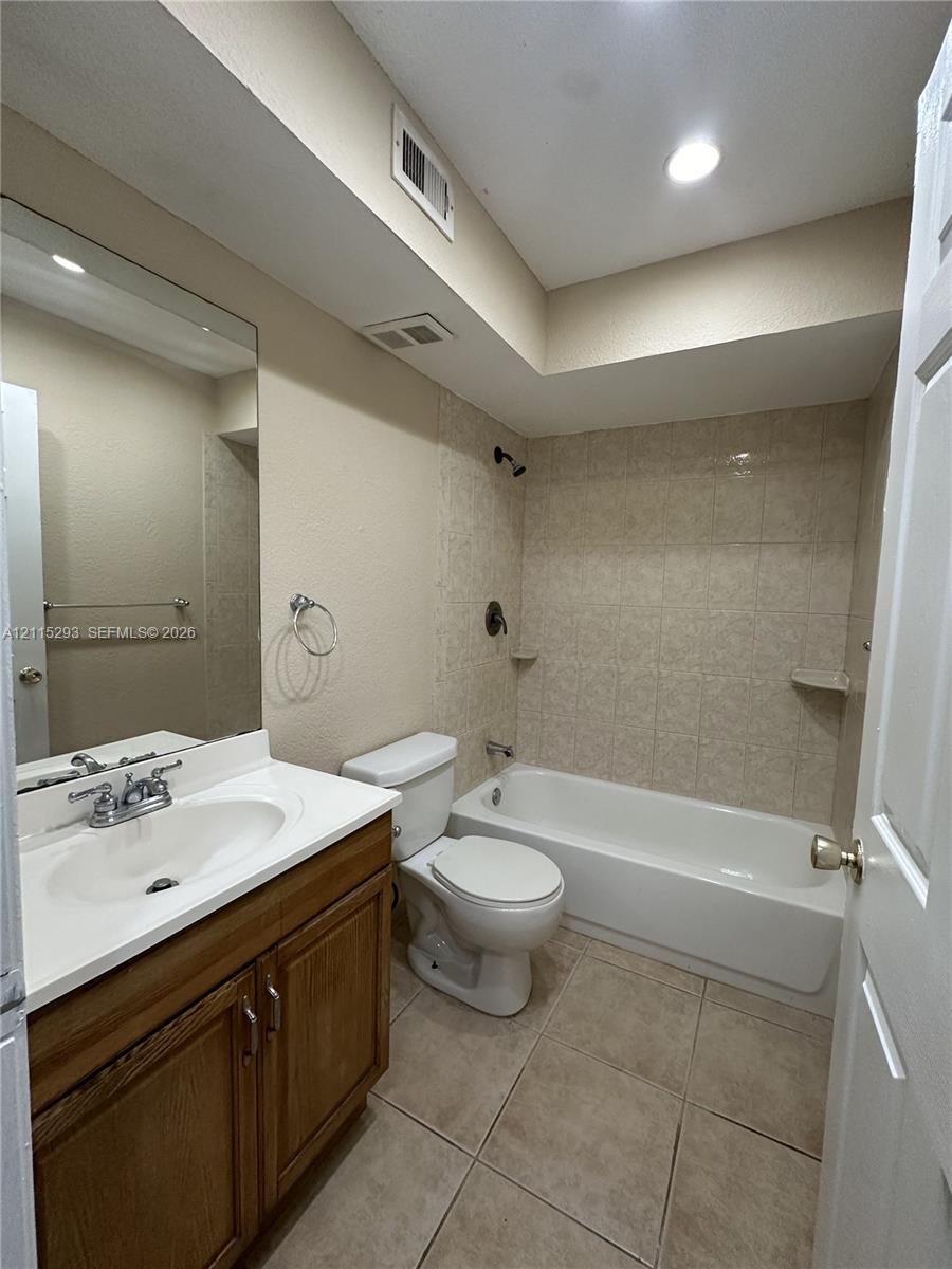 Bathroom featuring a wood-finish vanity with a white countertop, large wall-mounted mirror, ceramic tile flooring, and a tiled tub-shower combination