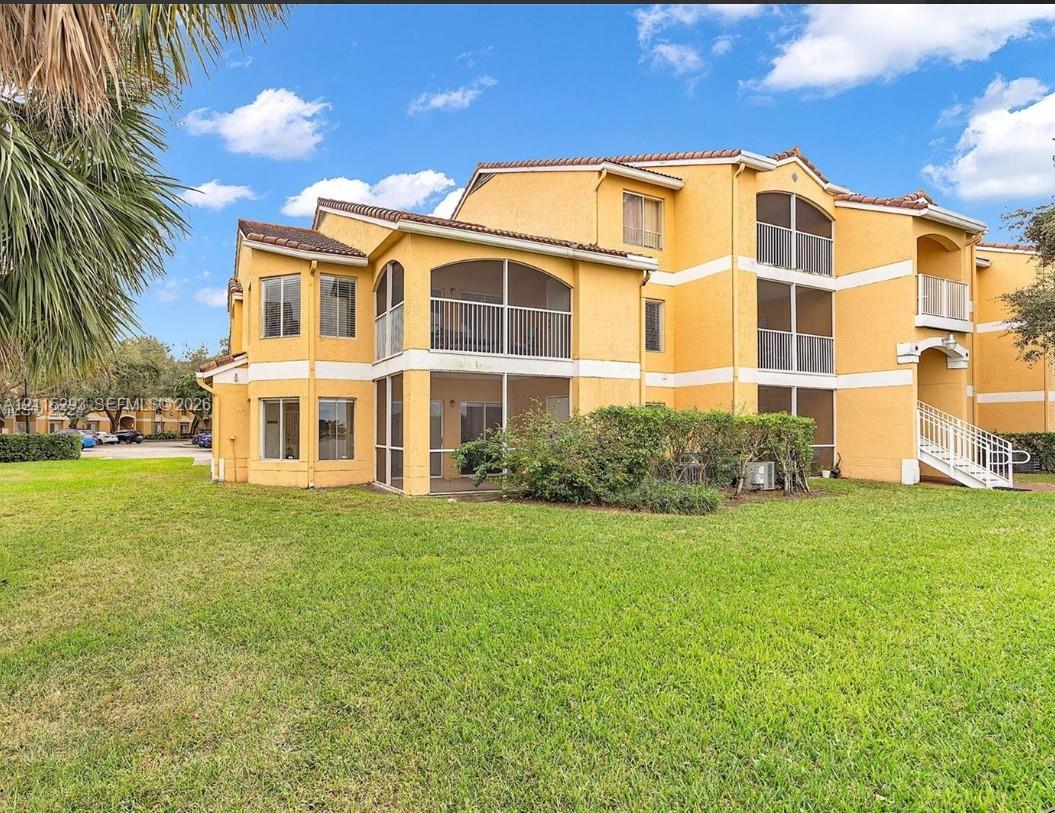 Stucco exterior featuring multi-level screened-in lanais, tile roofing, and metal stair railings, set against an expansive manicured lawn