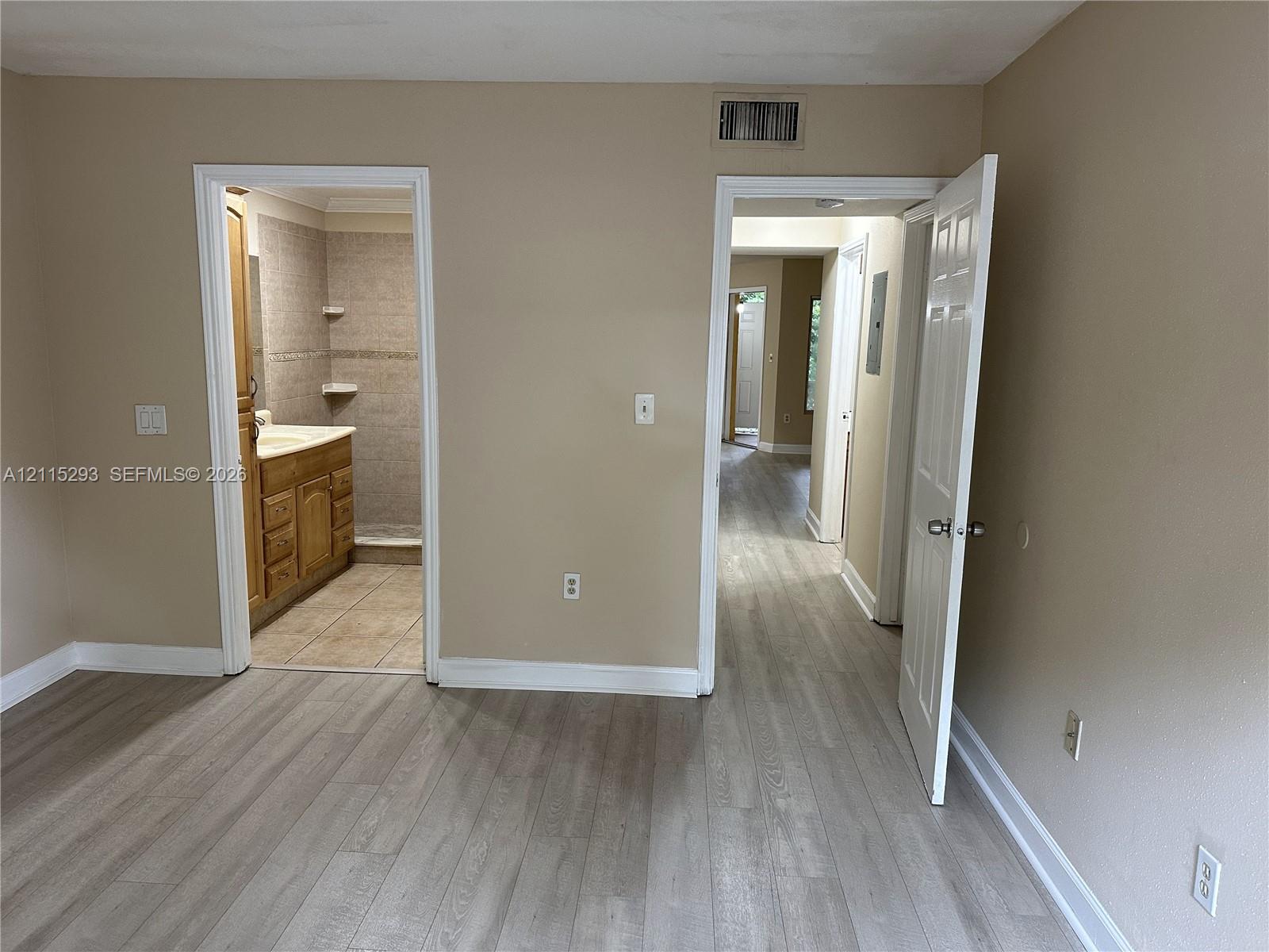 Wood-finish flooring, multi-panel interior doors, and a bathroom featuring wood-toned cabinetry and neutral wall-mounted shelving