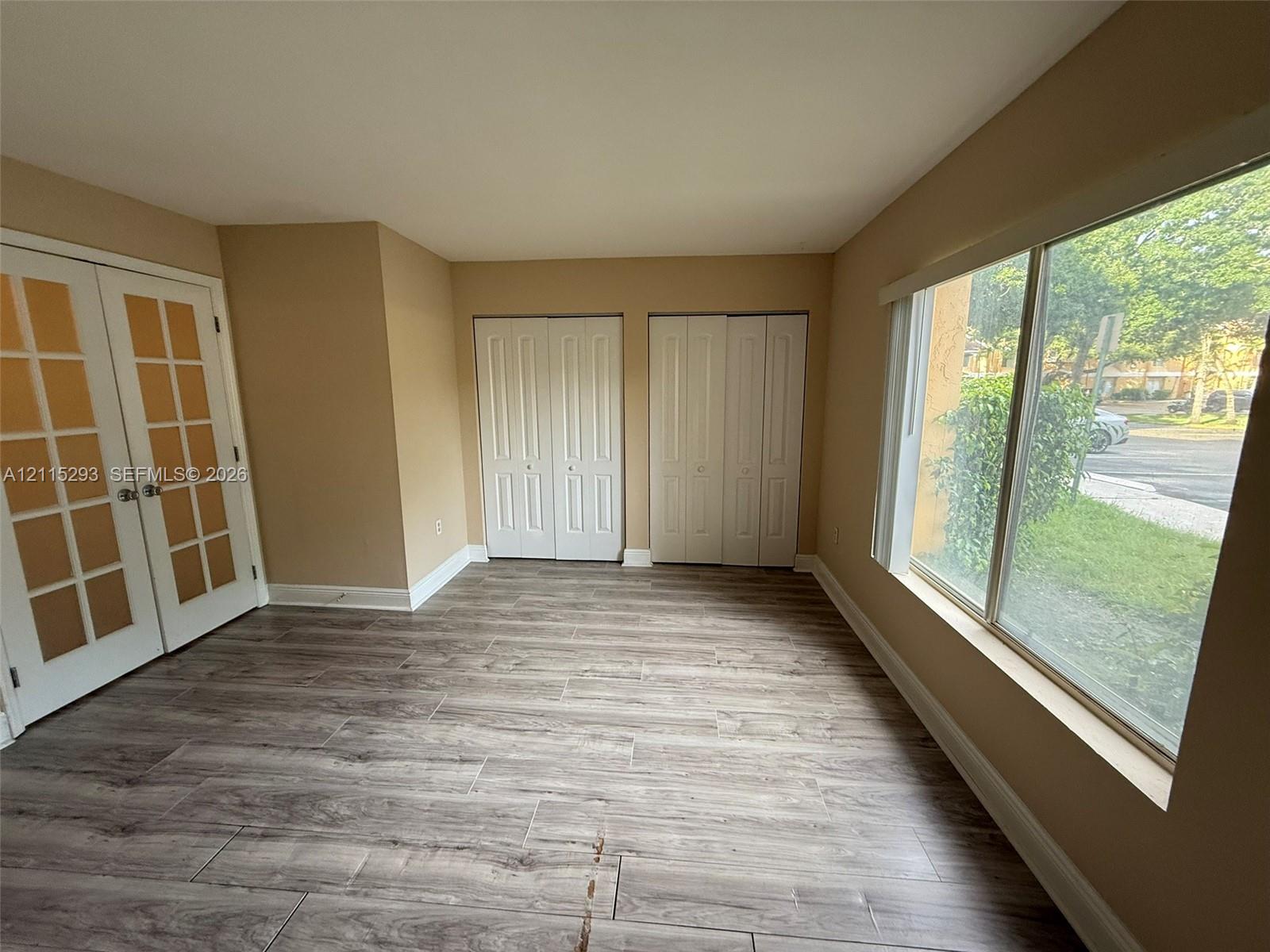 Wood-finish flooring, dual French doors with glass panes, two sets of bi-fold closet doors, and large windows