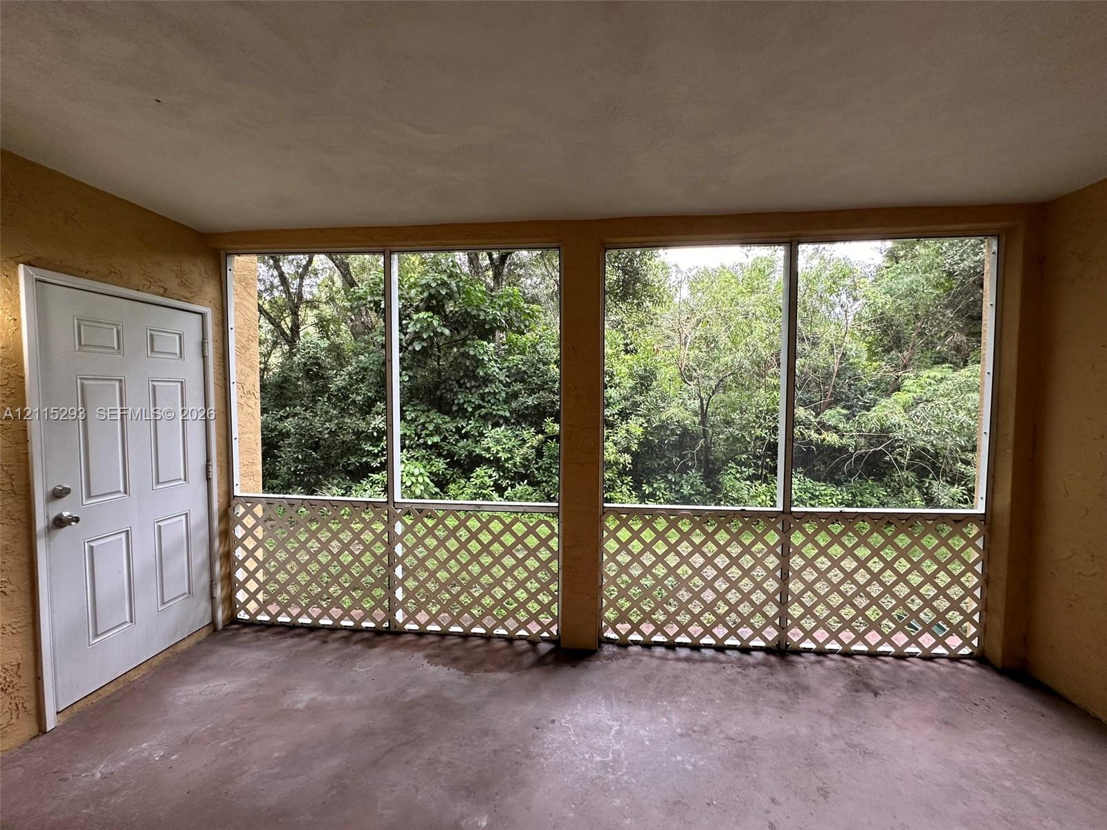Enclosed porch featuring floor-to-ceiling screens, decorative lattice accents, and a solid-core six-panel door