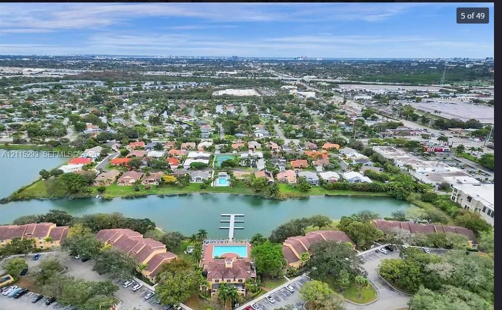 Aerial perspective of residential property featuring a waterfront location, private dock, swimming pool, tile roofing, and expansive grounds with mature landscaping