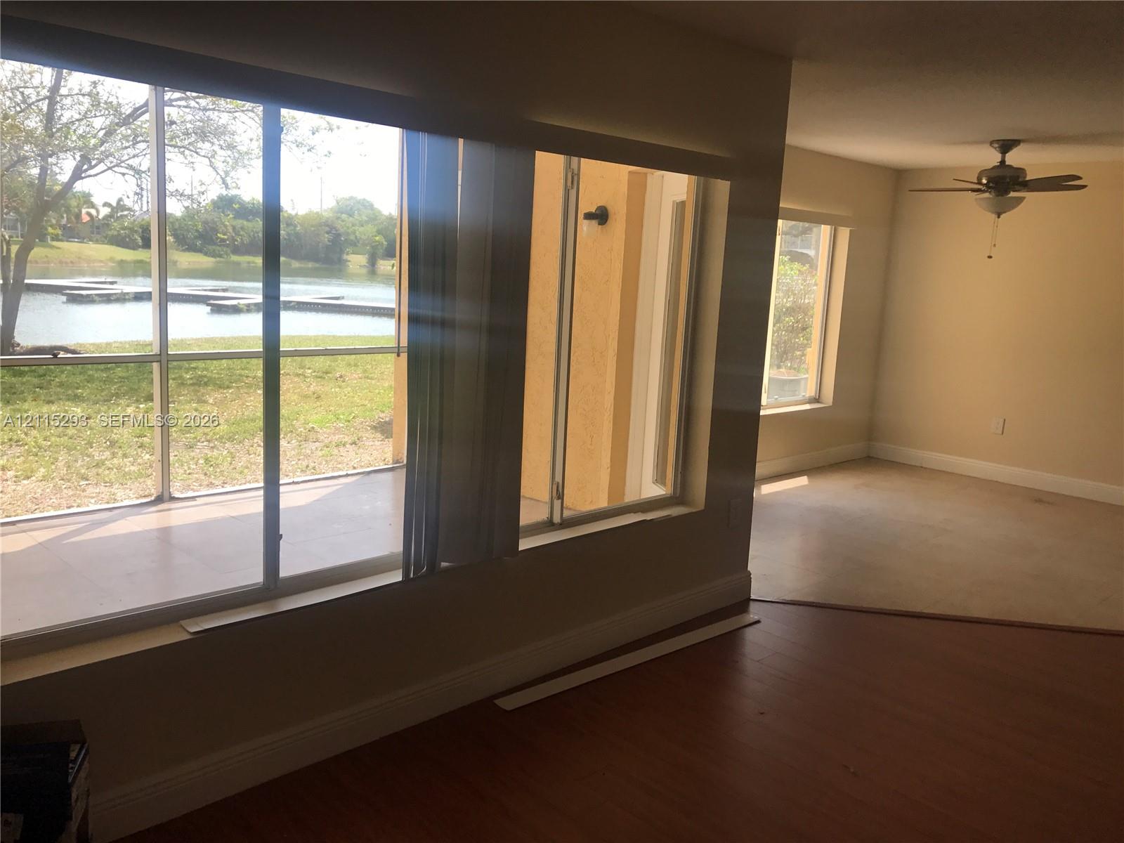 Screened-in patio with waterfront exposure, sliding glass doors, wood-finish flooring, and ceiling fan with integrated lighting