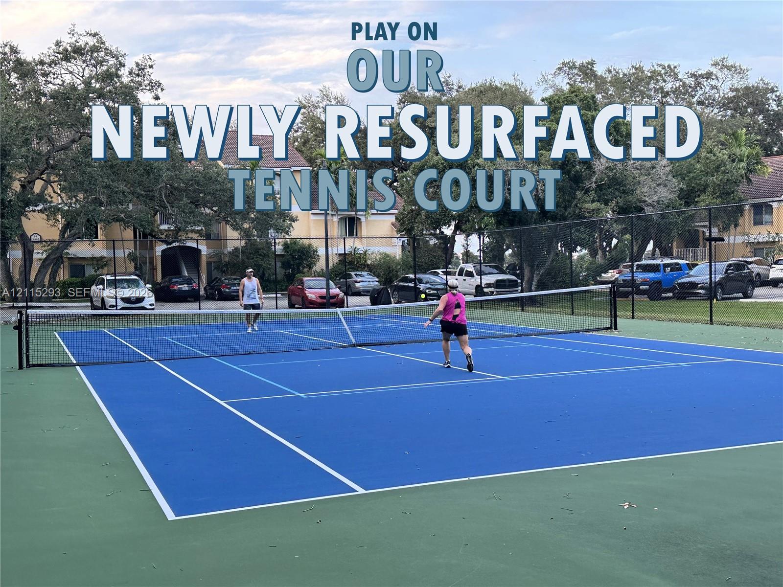 Tennis court featuring a high-contrast blue and green surface, permanent net, and perimeter chain-link fencing