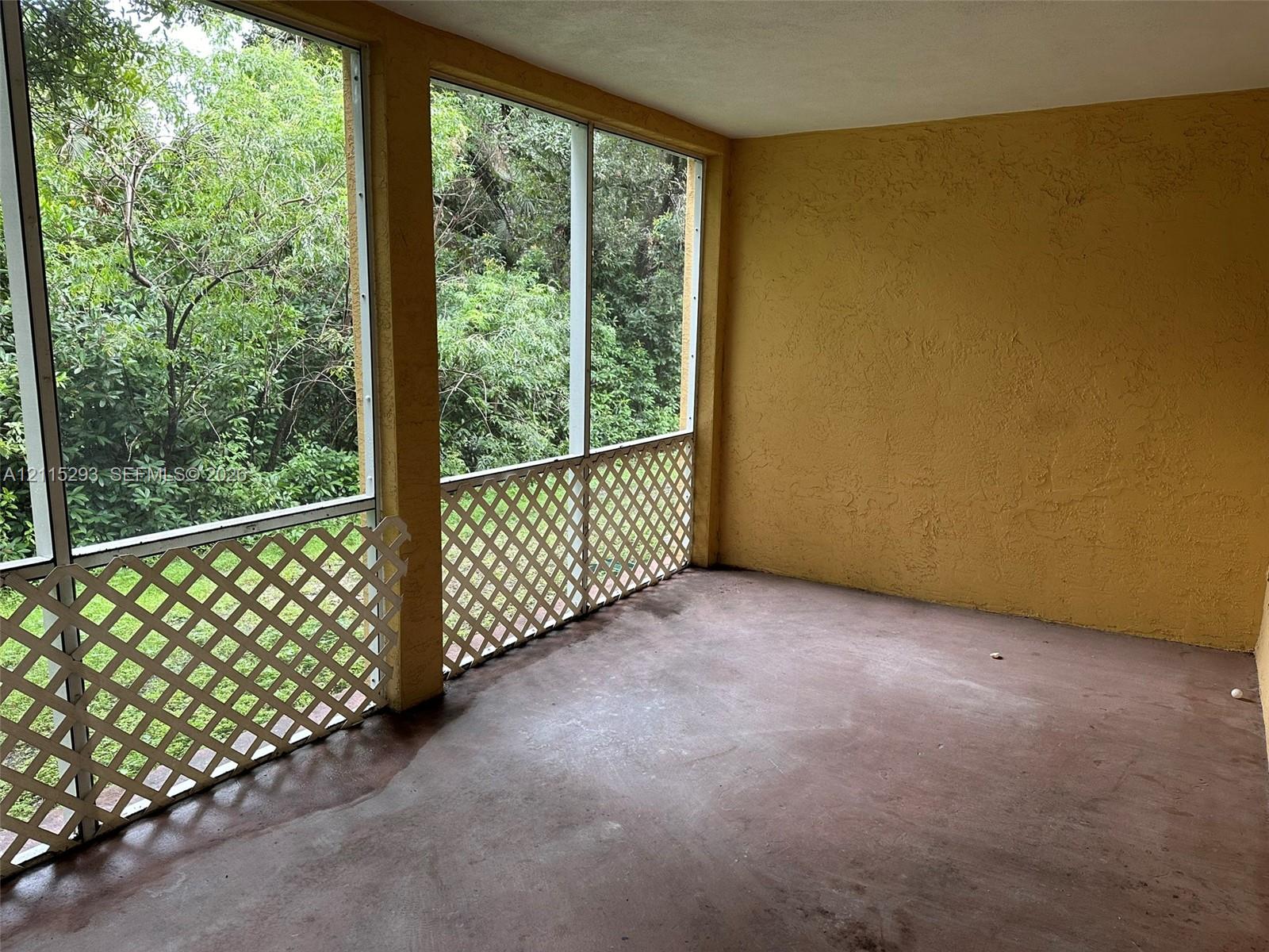 Screened-in porch featuring textured walls, concrete flooring, and white lattice paneling