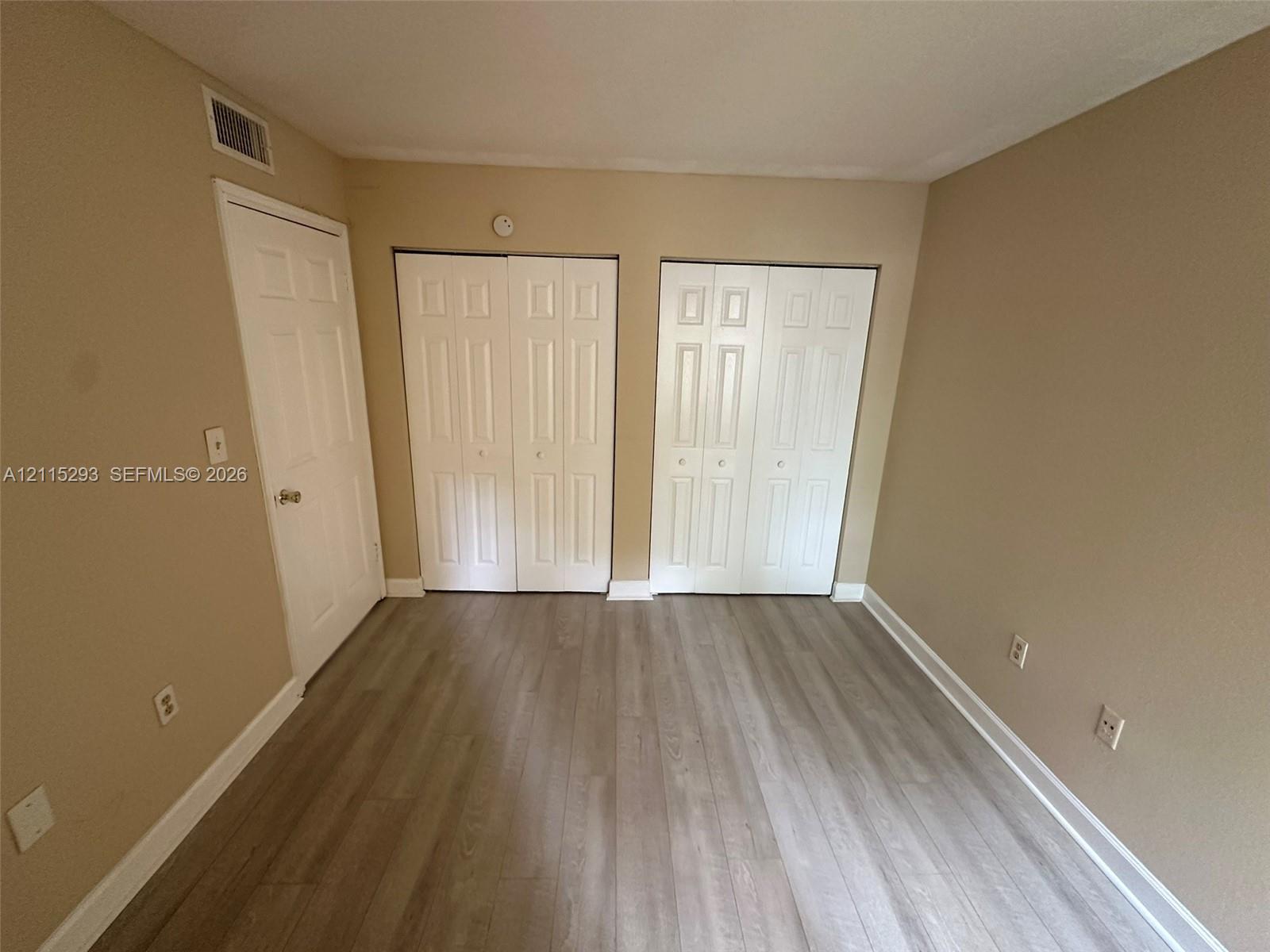 Room featuring neutral wall paint, wood-finish flooring, and dual bi-fold closet doors