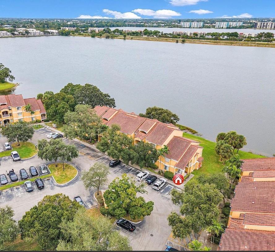 Aerial perspective of a multi-story building featuring terracotta-toned roof tiles, stucco exterior walls, paved surface parking, and waterfront positioning